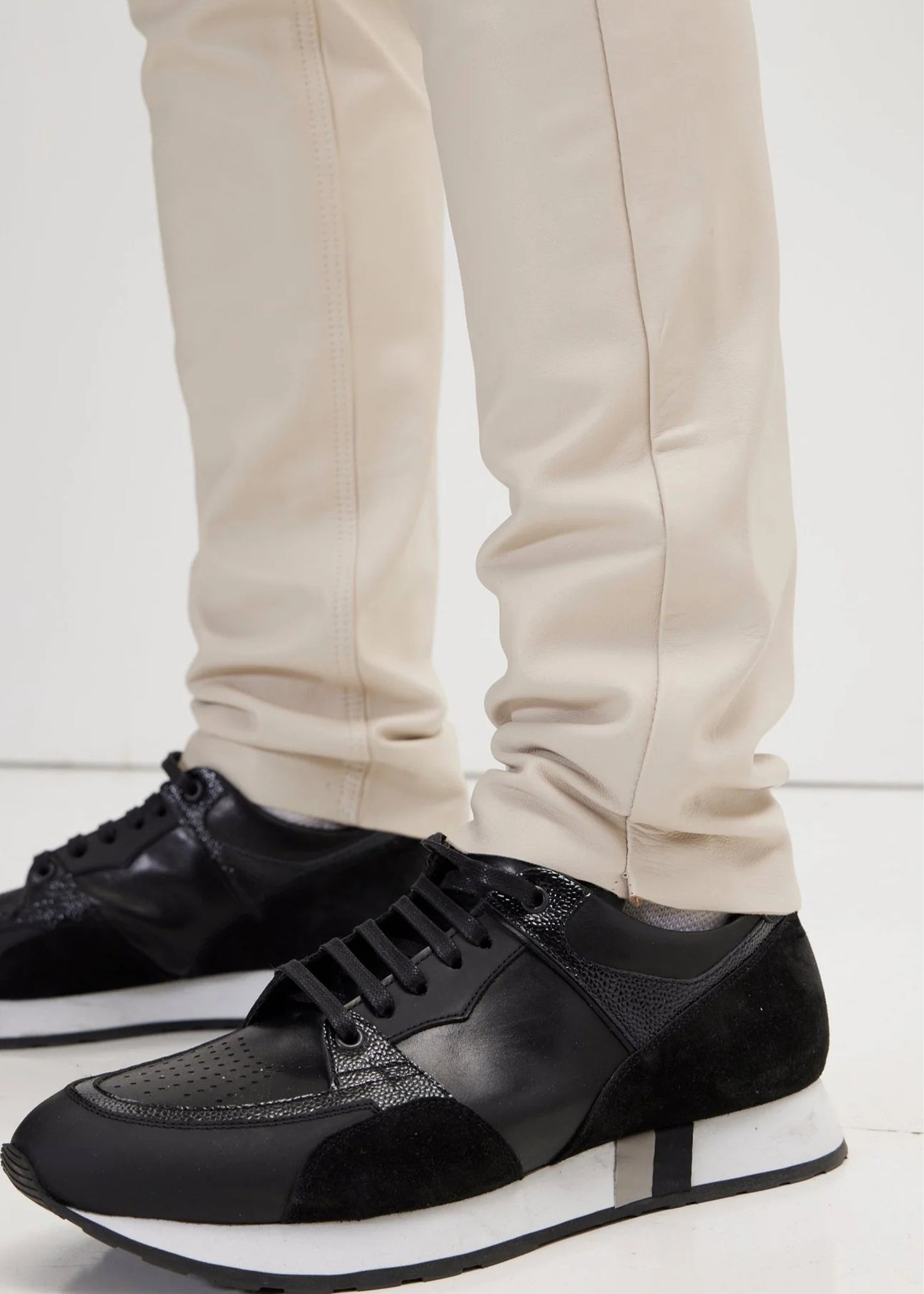 Black sneakers worn with beige pants on a white background