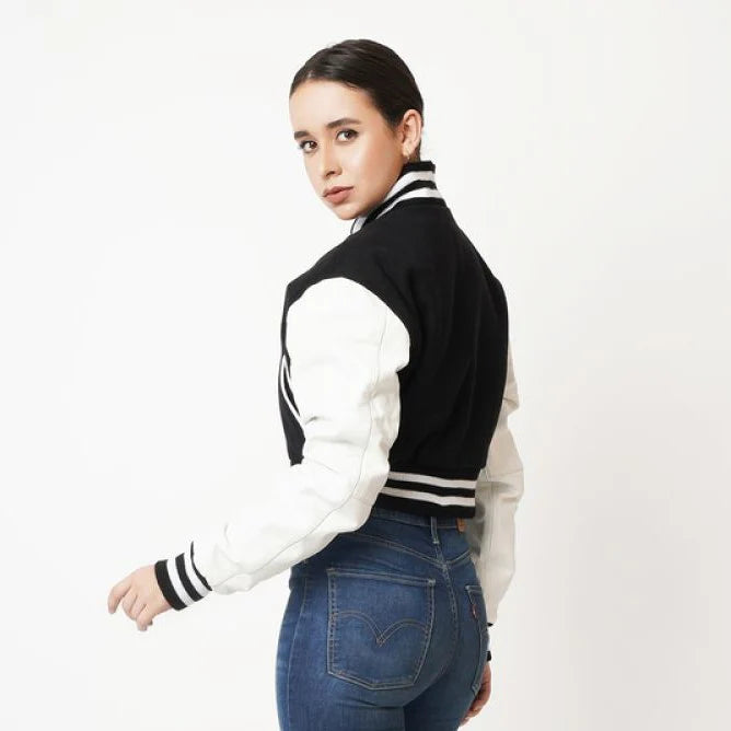 Person wearing a black and white varsity jacket with blue jeans on a white background