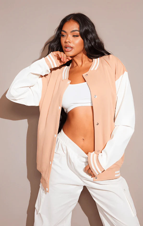 Woman wearing a beige varsity jacket over a white outfit against a plain background