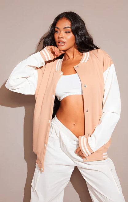 Woman wearing a beige varsity jacket over a white outfit against a plain background