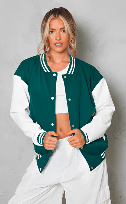 Woman wearing a green and white varsity jacket over a white outfit against a gray background
