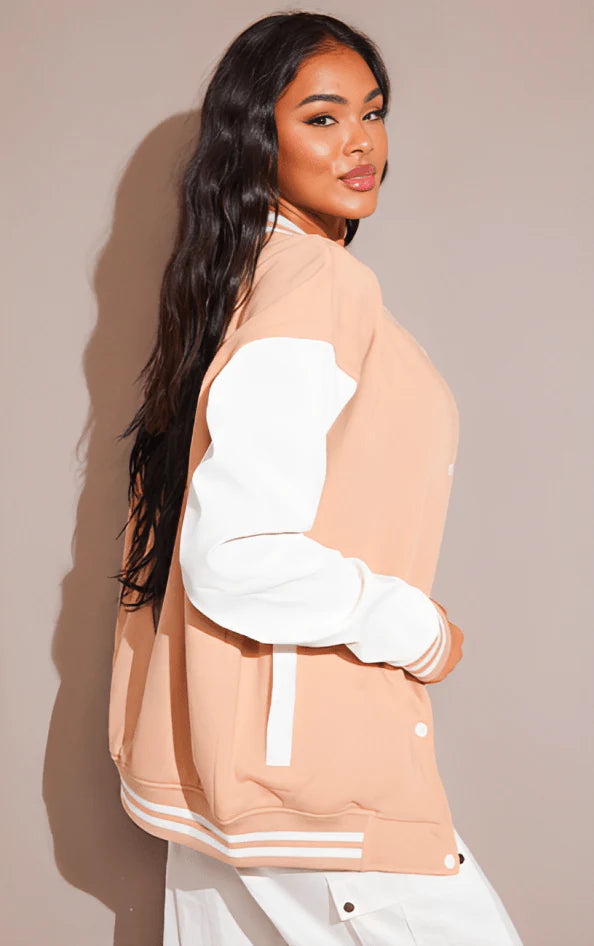 Woman wearing a beige and white varsity jacket against a plain background