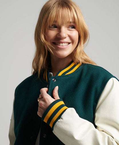 Woman wearing a green and white varsity jacket with yellow accents on a plain background