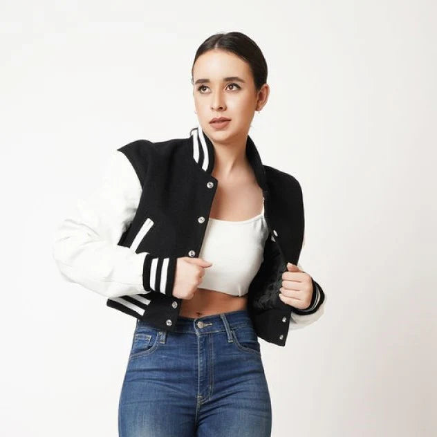 Woman wearing a black and white varsity jacket with blue jeans on a white background