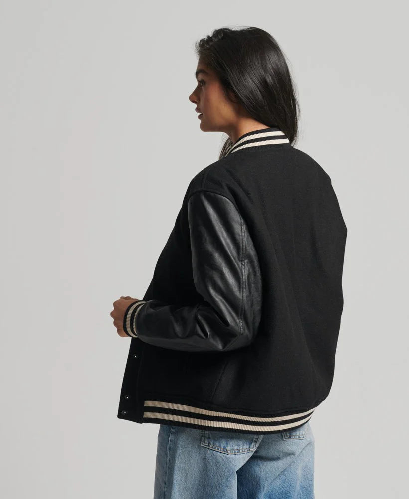 Person wearing a black varsity jacket with leather sleeves on a gray background