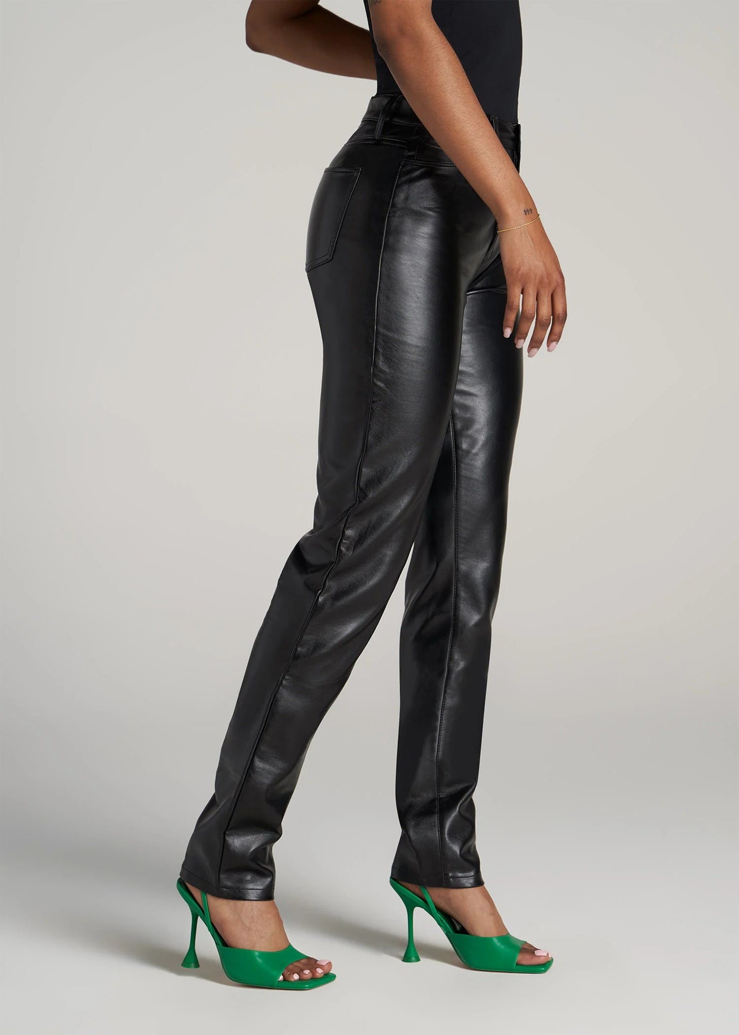 Person wearing black leather pants and green high heels on a plain background
