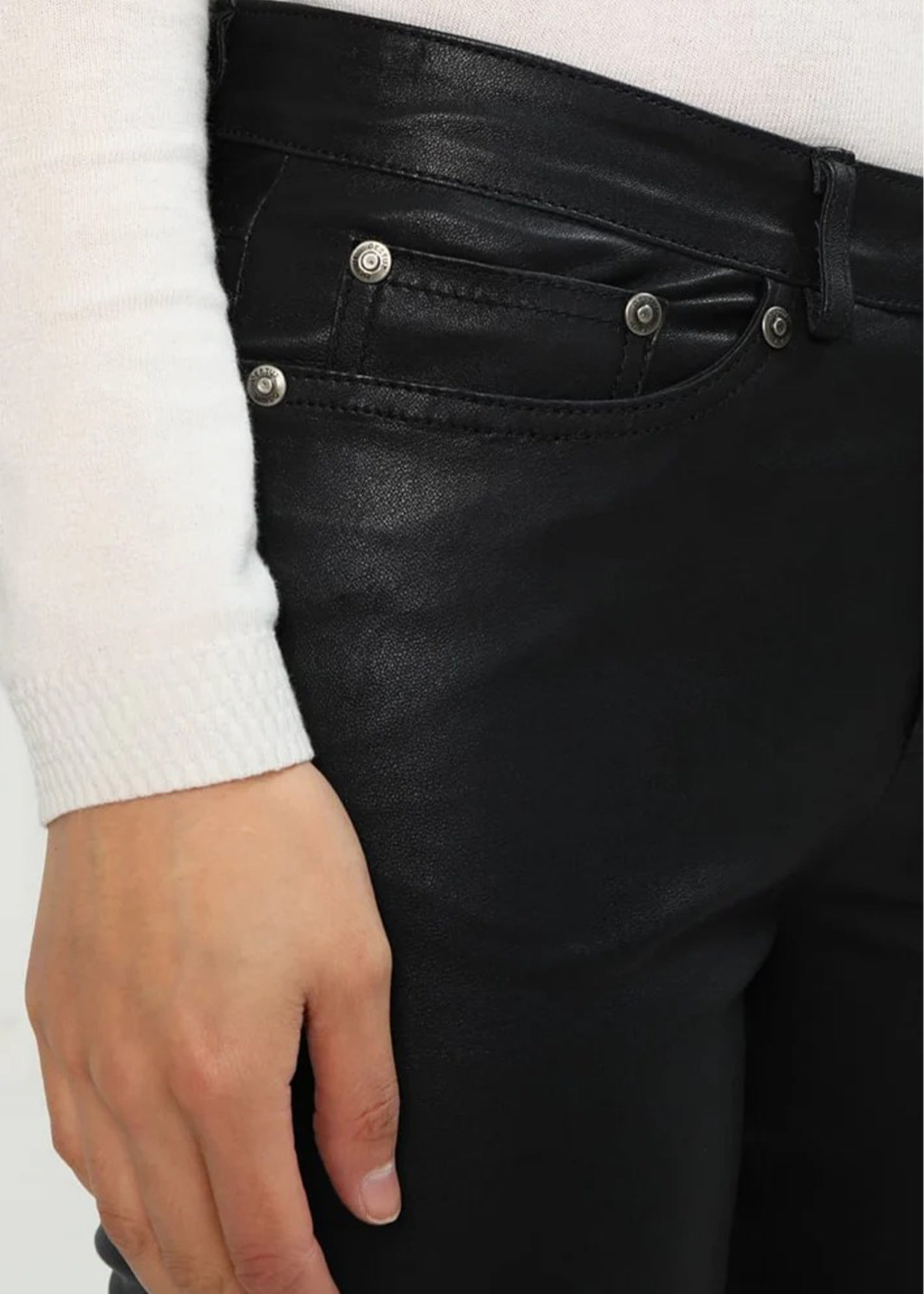 Close-up of black leather pants with a white sleeve and hand visible.