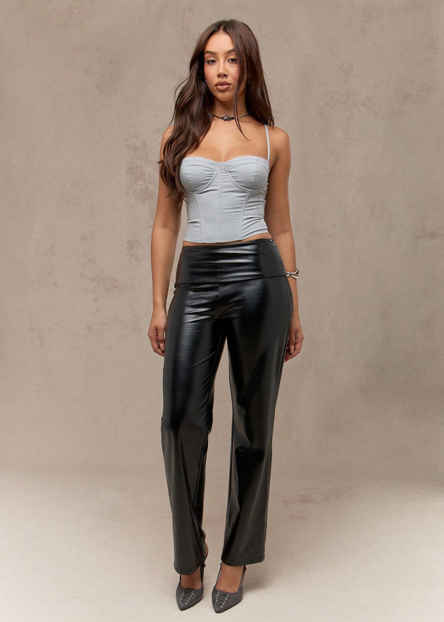 Woman wearing a light blue top and black leather pants against a neutral background