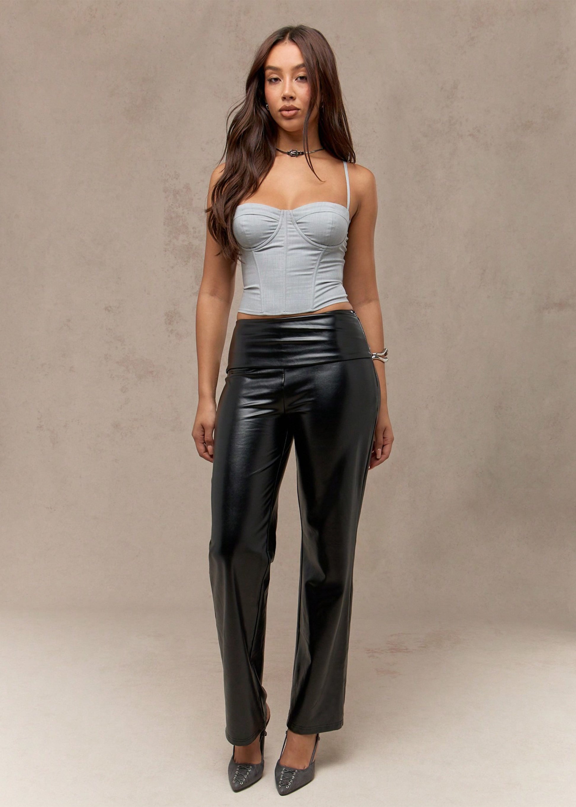 Woman wearing a light blue top and black leather pants against a neutral background