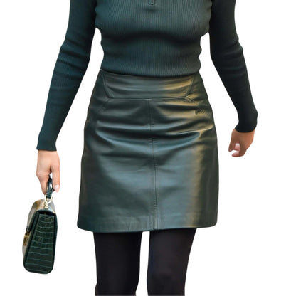 Person wearing a green leather skirt and black top on a white background