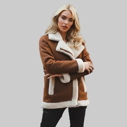 Woman wearing a brown shearling coat standing on a checkered floor with posters on the wall.