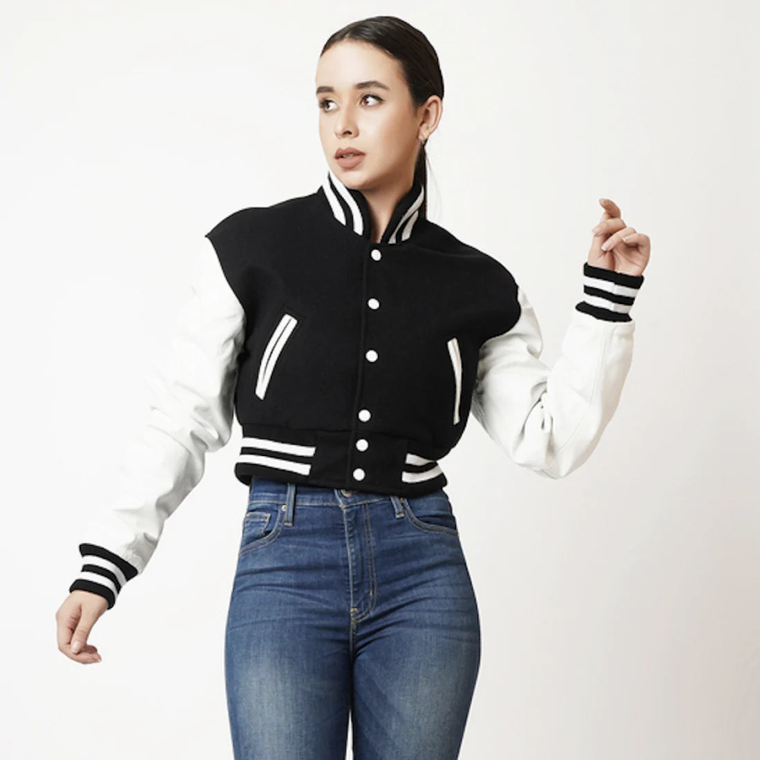 Woman wearing a black and white varsity jacket with blue jeans on a white background