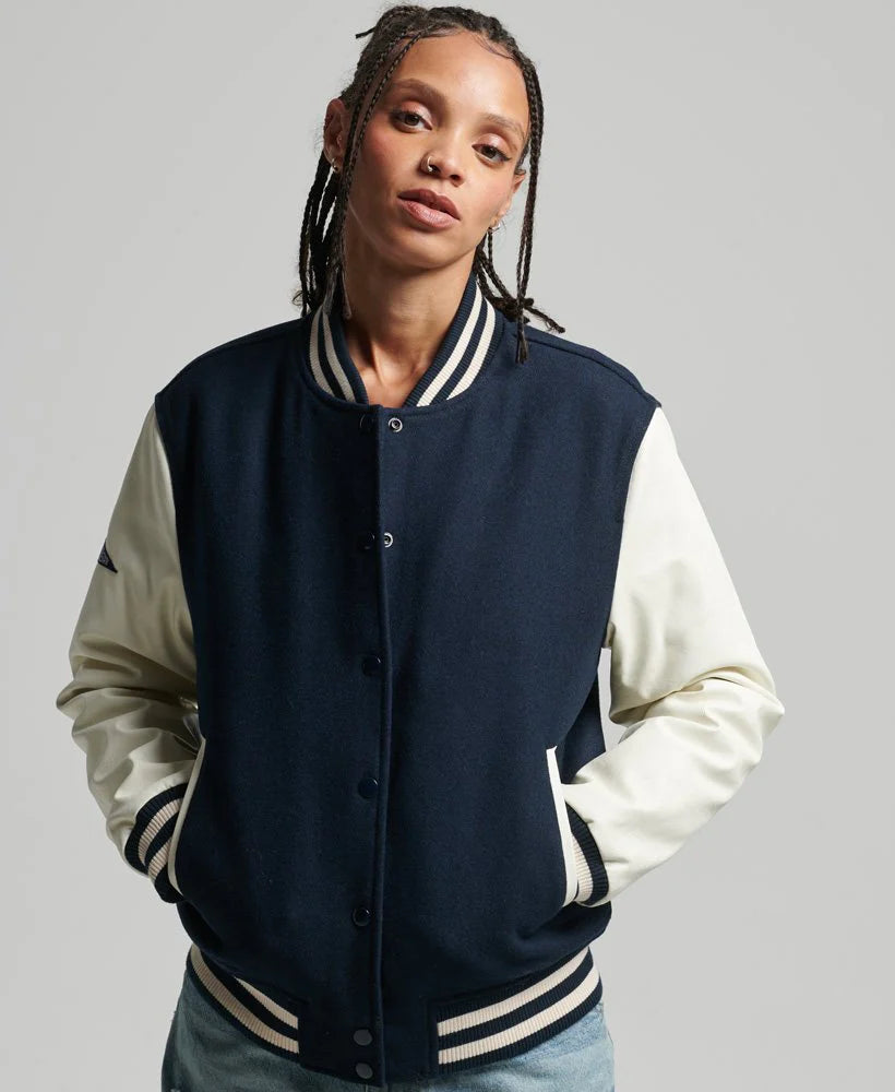 Person wearing a navy and white varsity jacket on a gray background