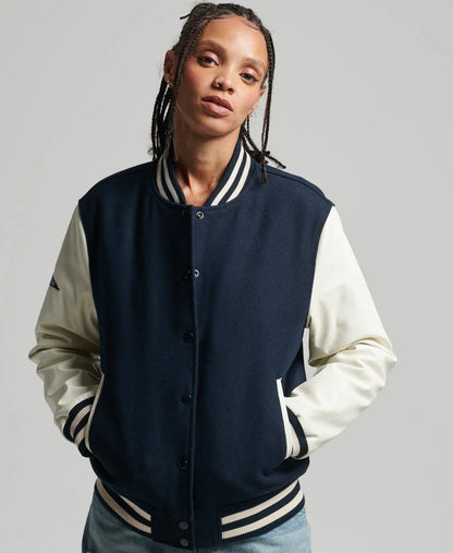 Person wearing a navy and white varsity jacket on a gray background