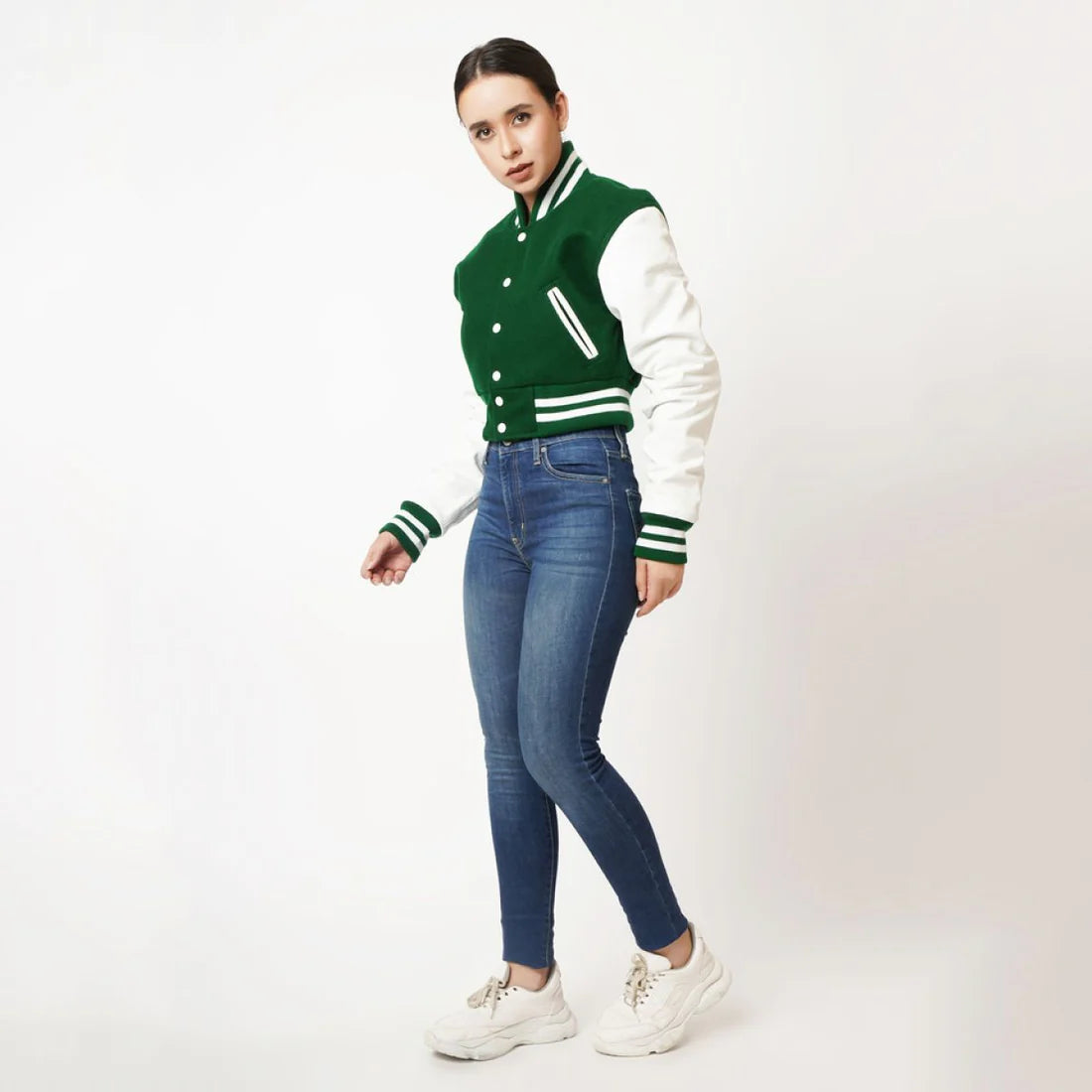 Person wearing a green and white varsity jacket with blue jeans on a white background