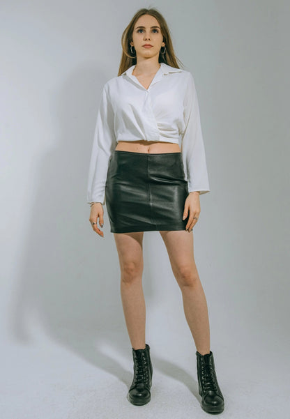 Woman wearing a white blouse, black leather skirt, and black boots on a plain background