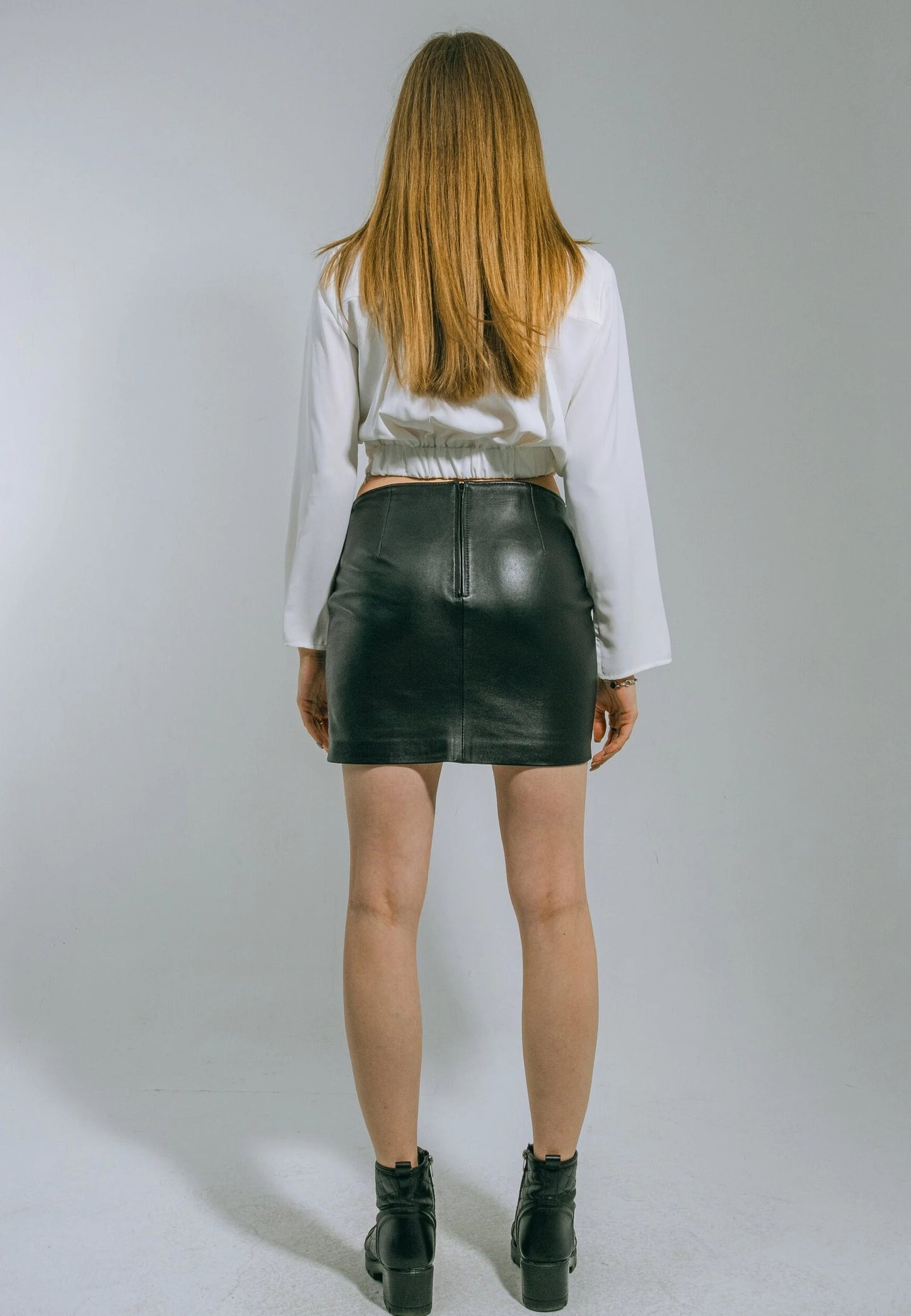 Person wearing a white blouse and black leather skirt on a plain background