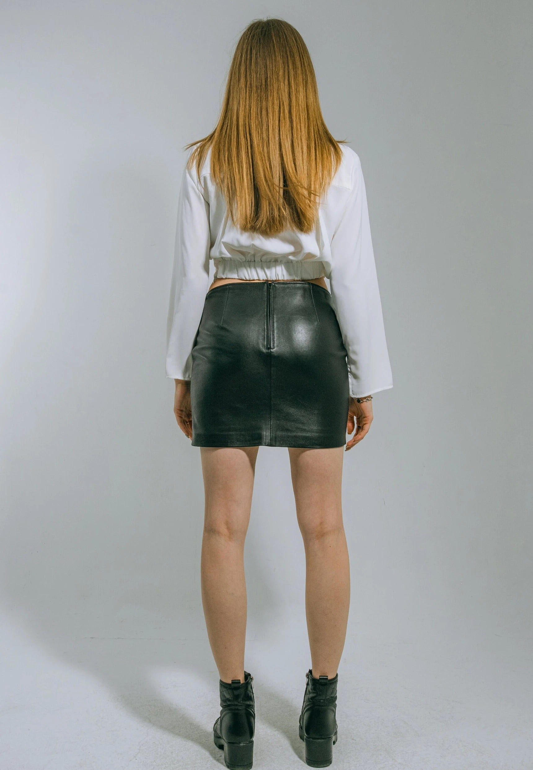 Person wearing a white blouse and black leather skirt on a plain background