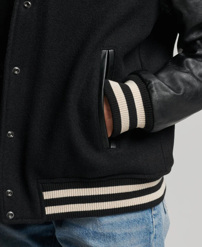 Black varsity jacket with white stripes on cuffs and waistband, worn over a leather jacket.
