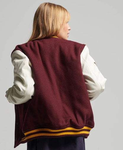 Person wearing a maroon varsity jacket with white sleeves on a gray background